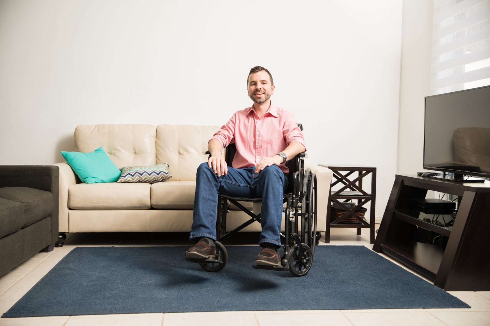 Optimistic man in a wheelchair smiling at the camera while relaxing at home