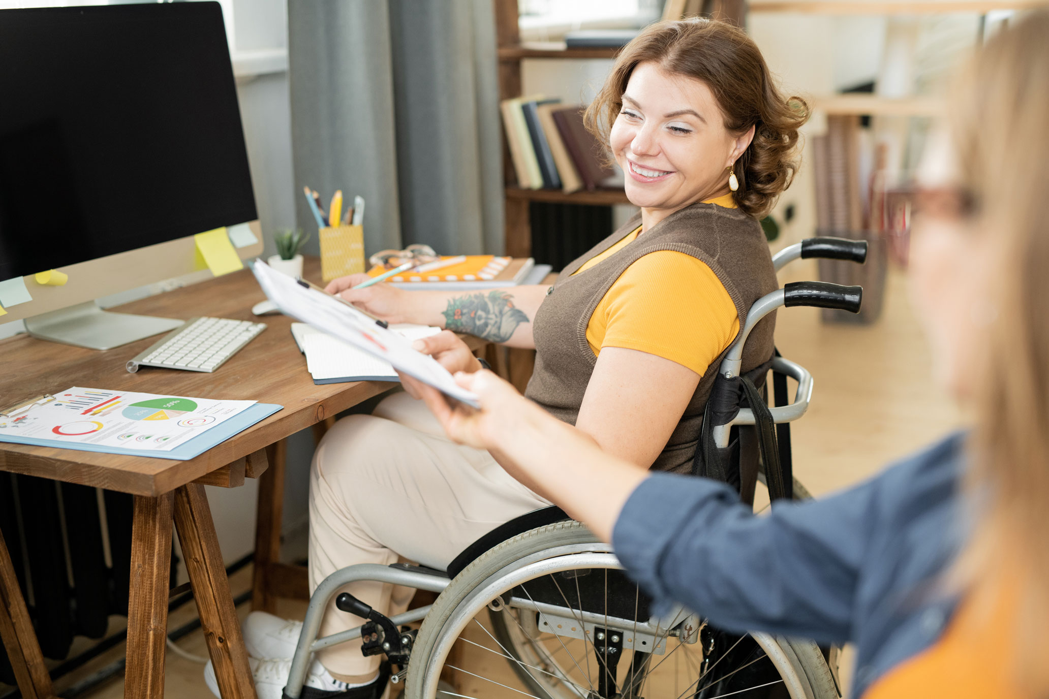 Woman in wheelchair working at computer and turning to take document