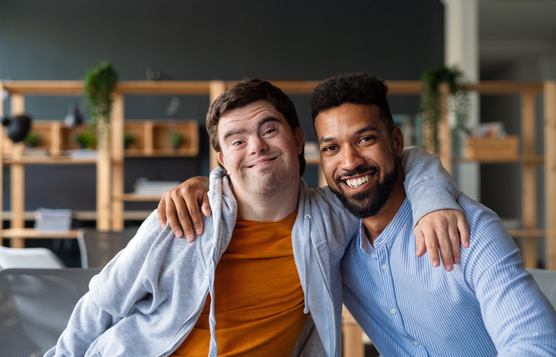 Young man with Down's Syndrome with support worker, arms around each other, looking to camera